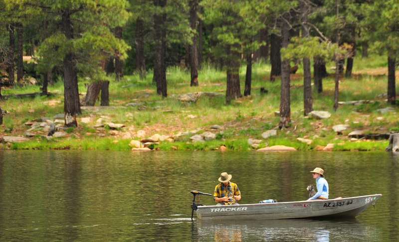 Two anglers in a small boat near the pine-lined shore of Woods Canyon Lake