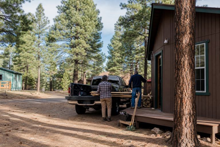 Neighbors unloading tools and lumber beside a cabin in the pines